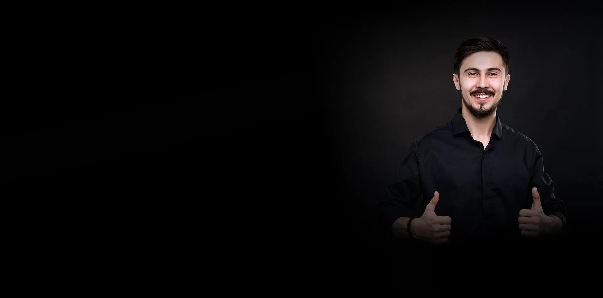 A smiling man giving two thumbs up against a black background